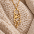 Personlig halskæde i guld med vedhæng formet som en baby og et lille hjerte med initial, liggende på lyst strikket stof.